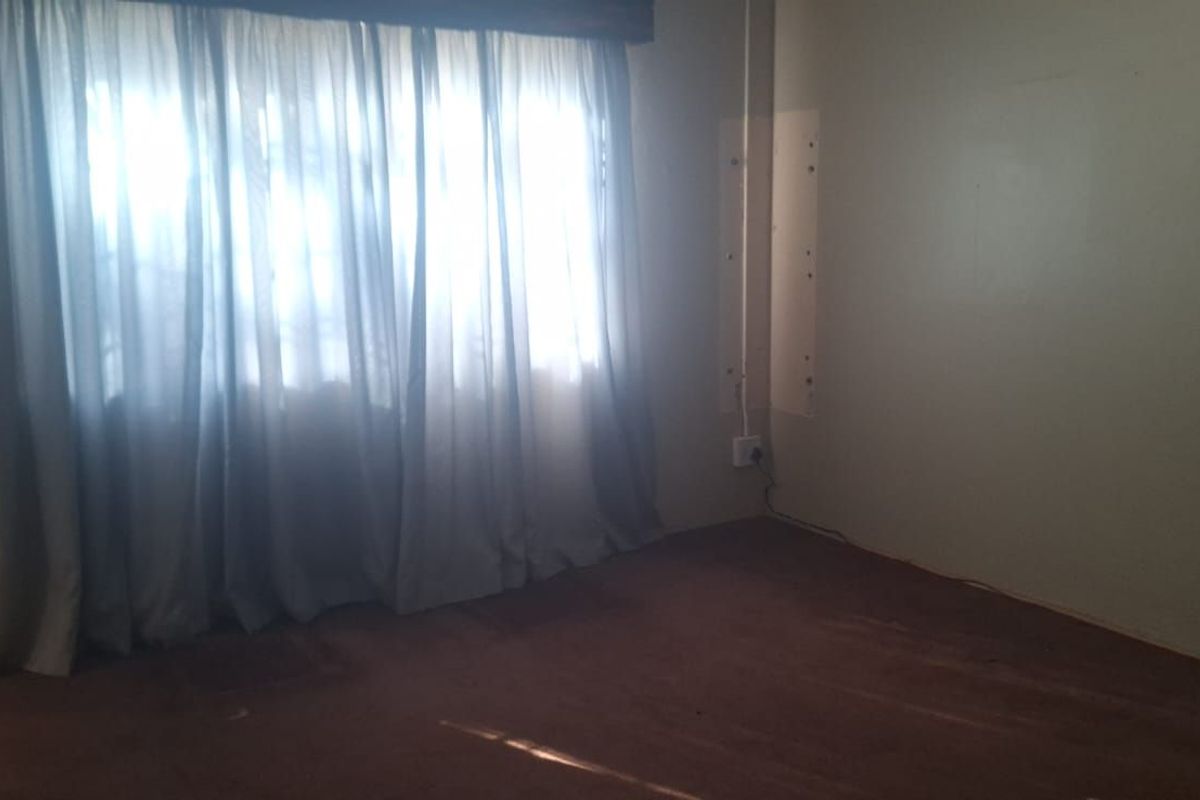 A vacant bedroom featuring carpet flooring, large window with curtains, and visible electrical conduit, offering a blank canvas for renovation.