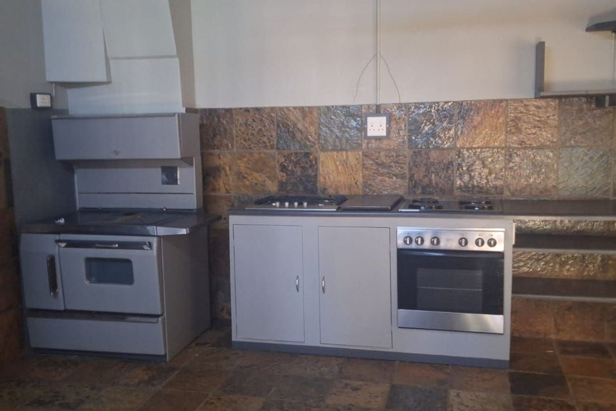 A dated kitchen area featuring stone-style wall tiles, built-in oven and hob, and basic cabinetry with exposed wiring and unfinished surfaces.