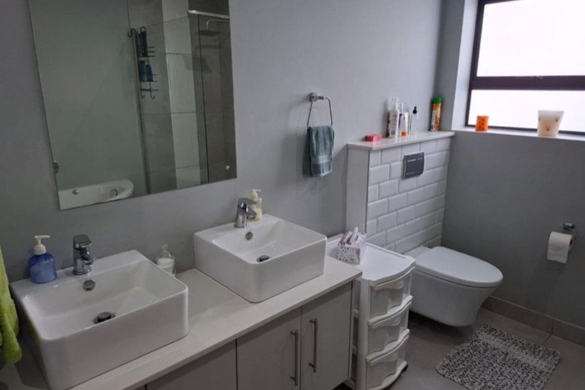 Modern bathroom featuring a double vanity with vessel sinks, wall-mounted toilet, and a glass-enclosed shower area with contemporary tiling.
