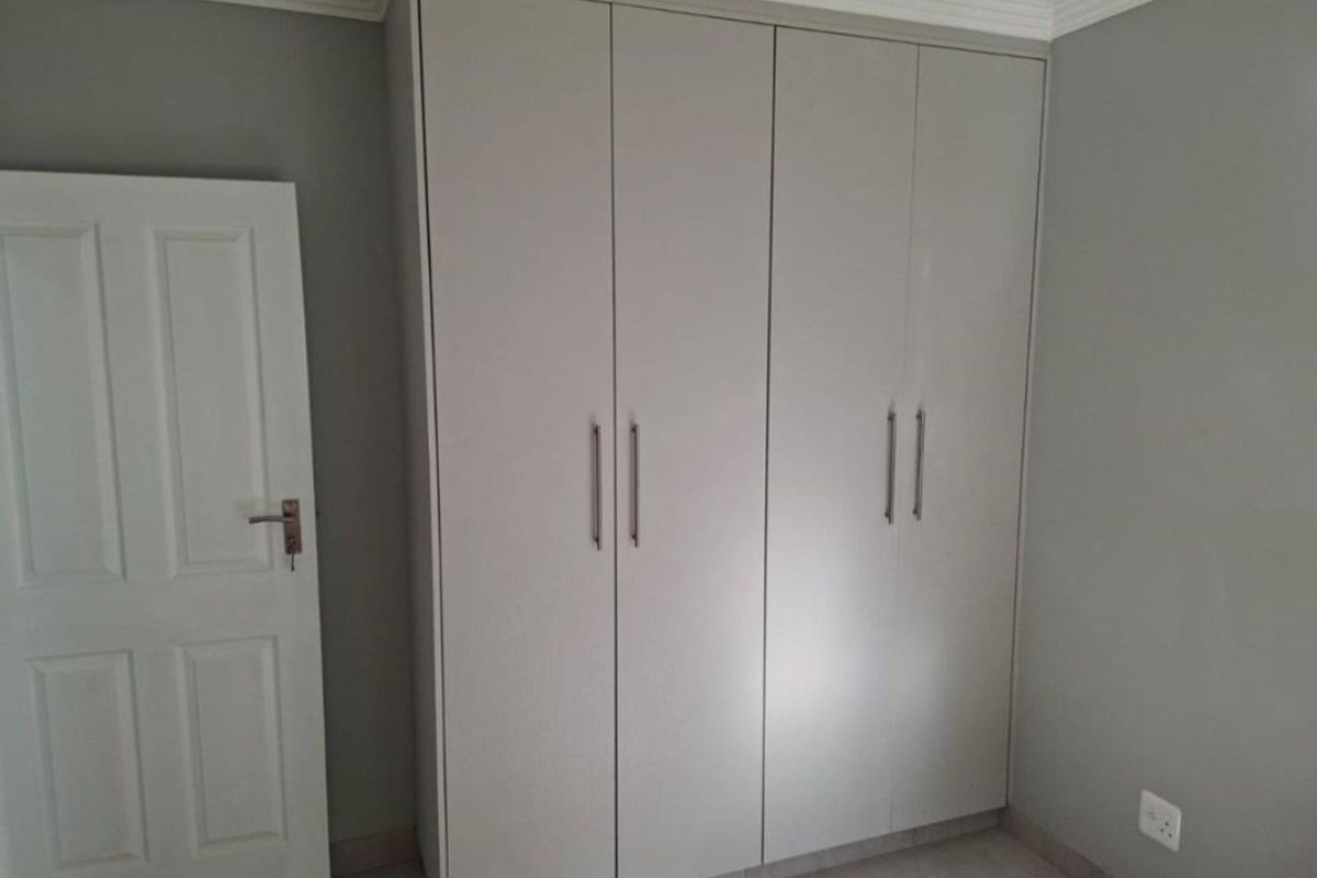 A bedroom featuring built-in floor-to-ceiling wardrobes with modern grey cabinetry and sleek metal handles, complemented by neutral wall tones and tiled flooring.