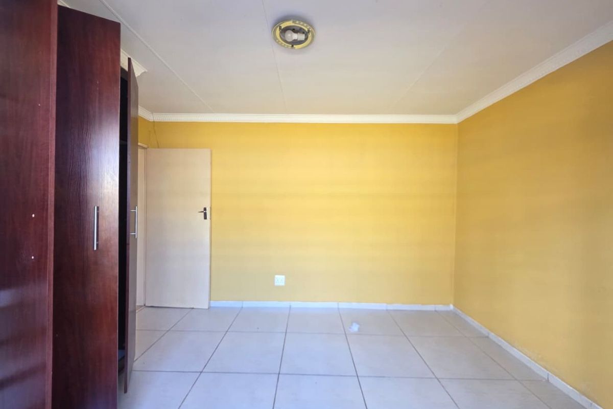 A bright, empty bedroom featuring tiled flooring, built-in wooden cupboards, and yellow painted walls, offering a clean and versatile space.