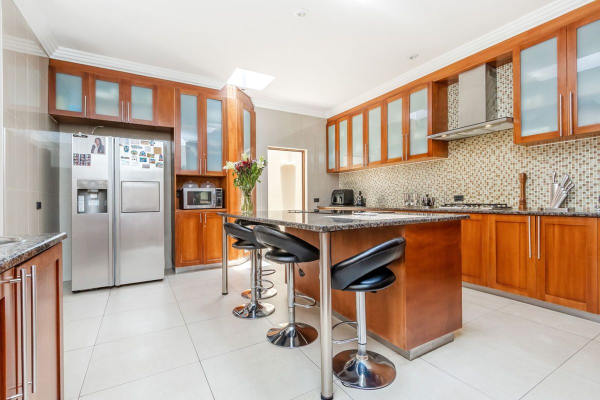 Spacious kitchen featuring warm-toned wooden cabinetry, granite countertops, a central island with breakfast bar seating, and a mosaic tile backsplash.