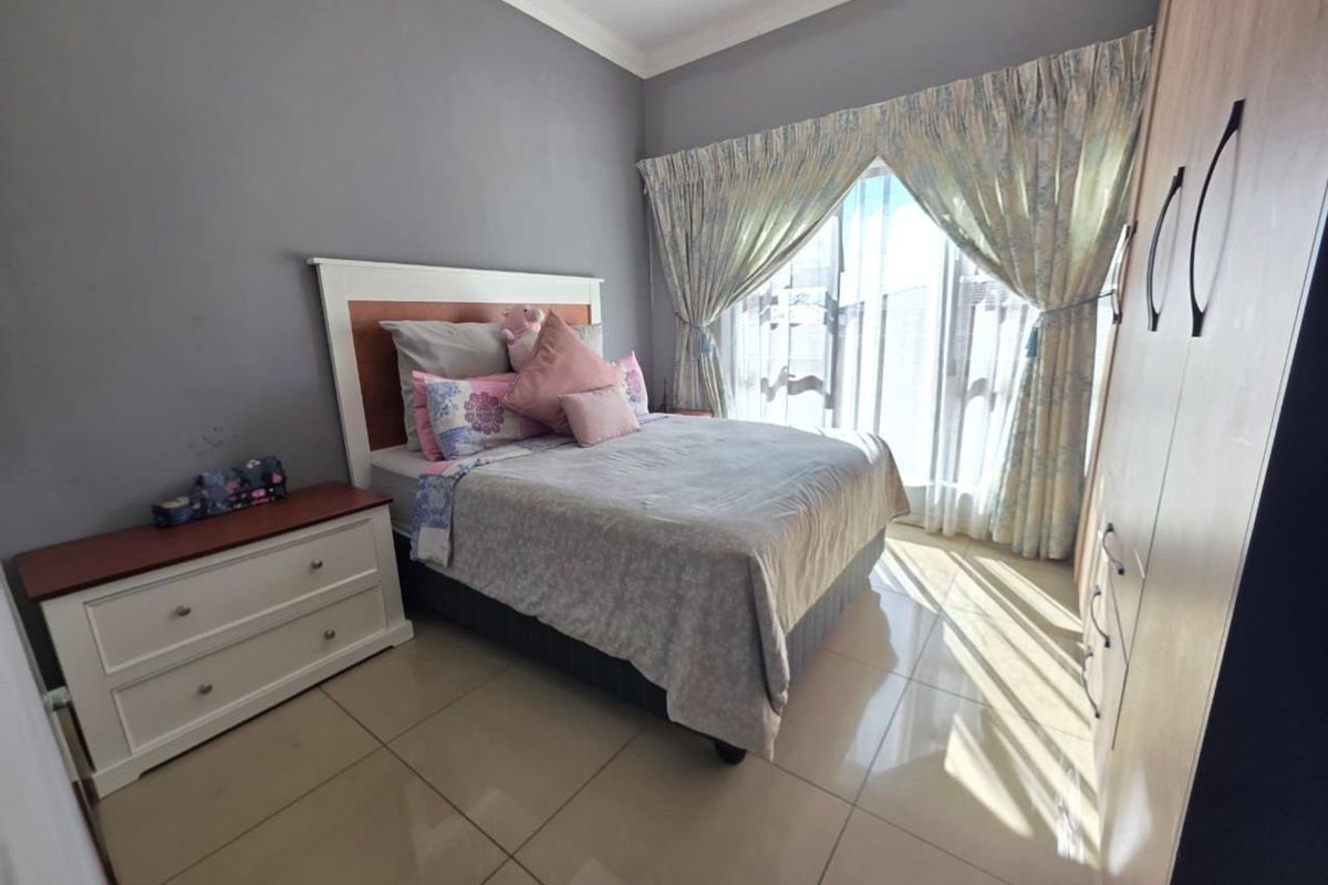 A well-lit bedroom featuring tiled flooring, built-in wooden cabinetry, and large sliding glass doors with curtains providing natural light.