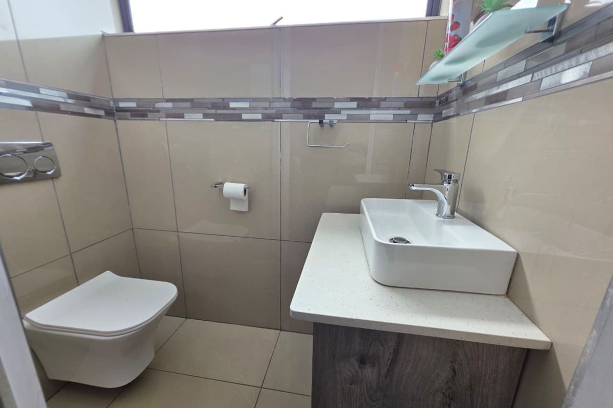 A modern bathroom featuring a wall-mounted toilet, a vessel sink set on a vanity cabinet, and neutral wall tiling with a decorative mosaic border.