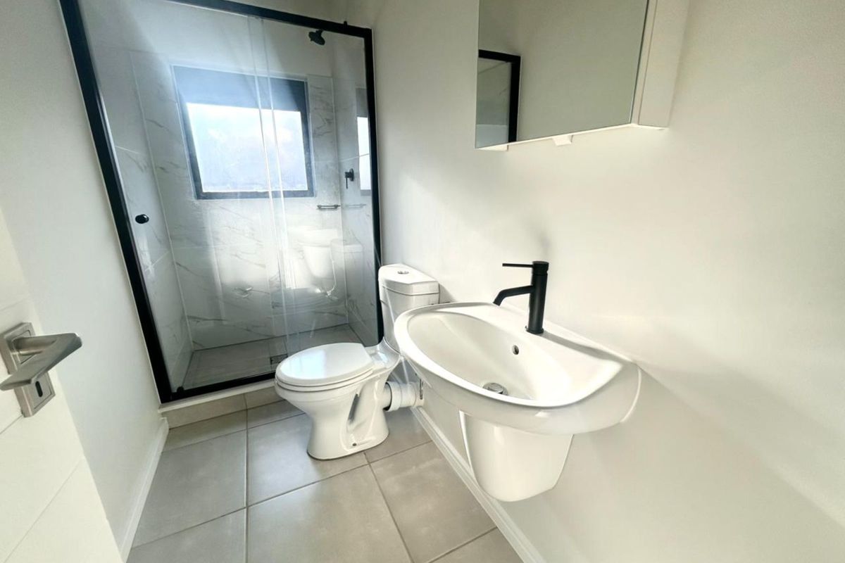 Modern bathroom featuring a walk-in shower with black frame, wall-mounted basin with black tapware, and a toilet.
