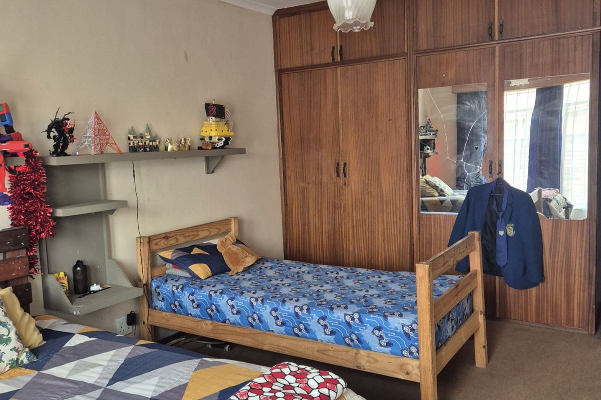 A bedroom featuring built-in wooden cupboards with a mirrored panel and floating shelving, providing functional storage space.