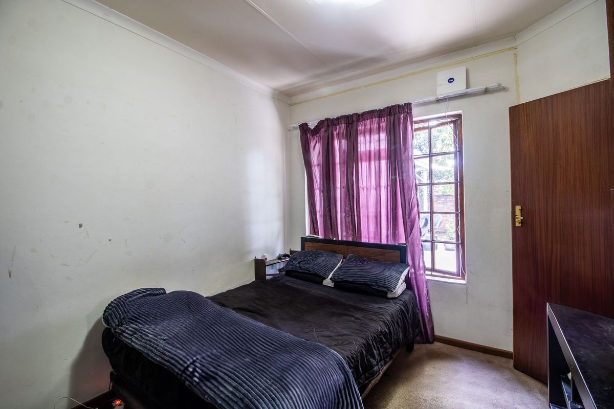 A bedroom featuring a window with security bars and a standard door, requiring cosmetic updates to the walls and flooring.