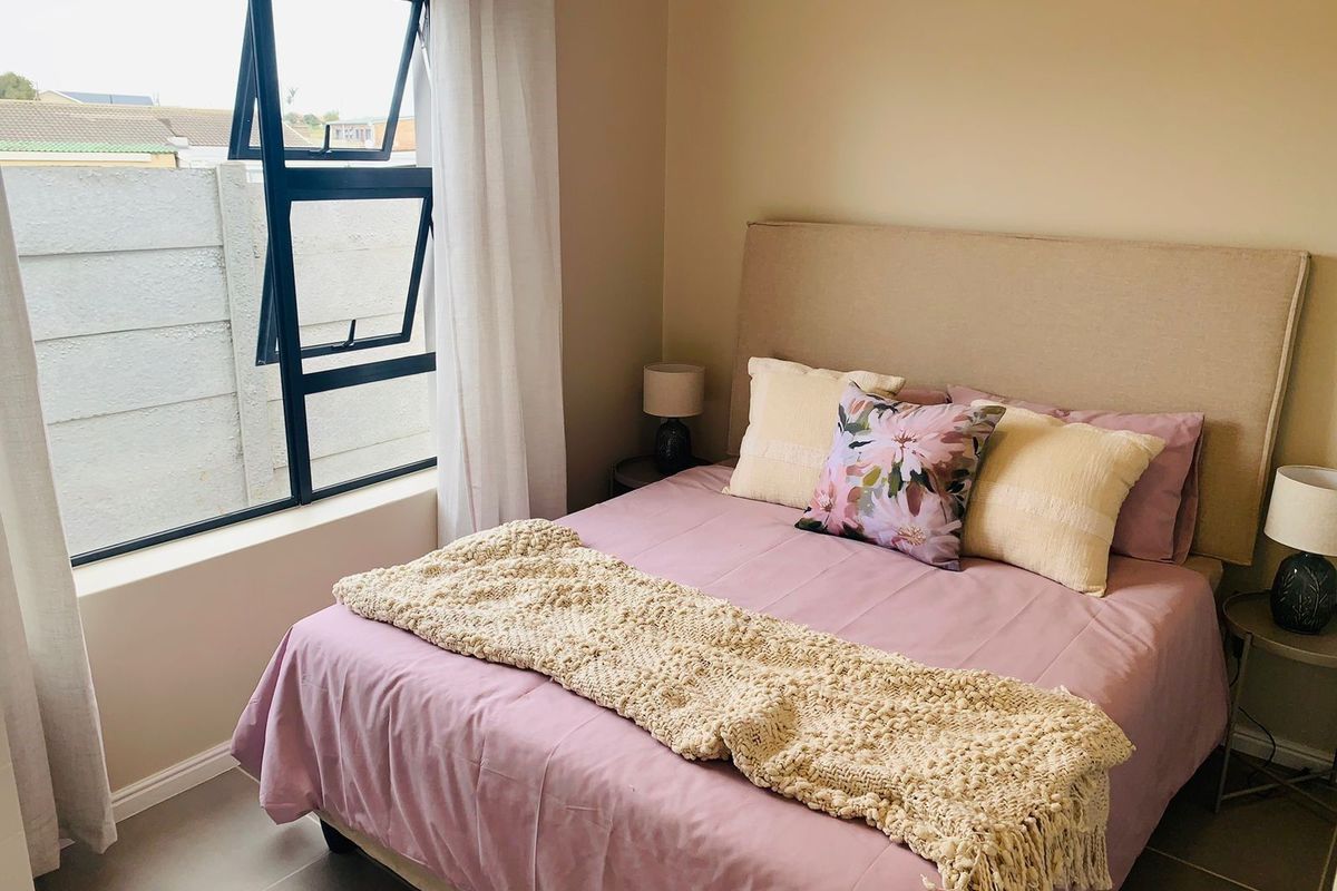 A well-maintained bedroom featuring neutral wall tones, tiled flooring, and a large aluminium-framed window providing natural light.