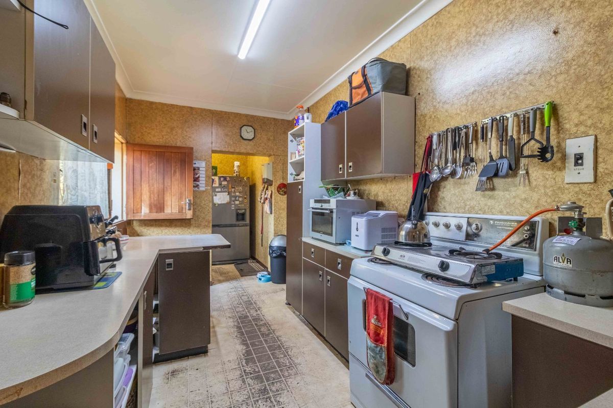 A functional kitchen featuring dated cabinetry, laminate countertops, and a freestanding gas stove, offering significant potential for modernization and renovation.