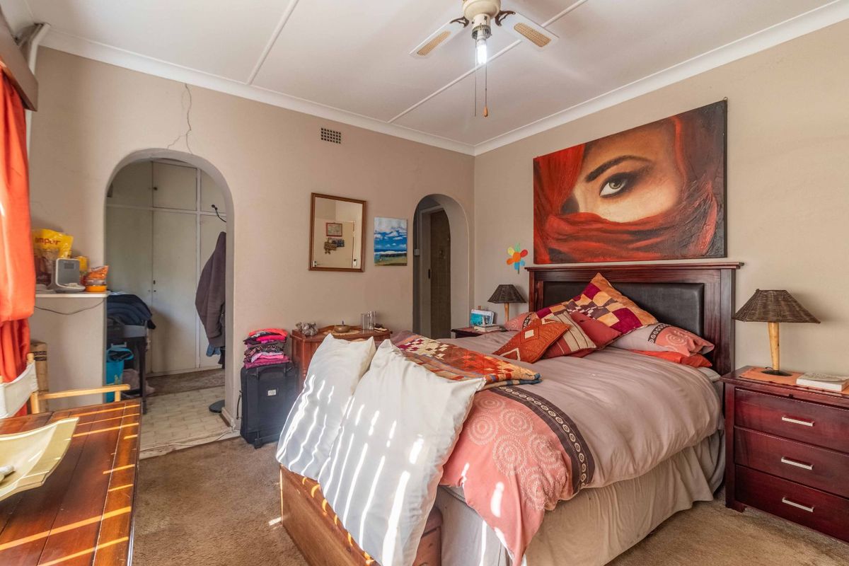 A bedroom featuring an arched entryway leading to built-in storage, a ceiling fan, and neutral wall finishes requiring minor maintenance.
