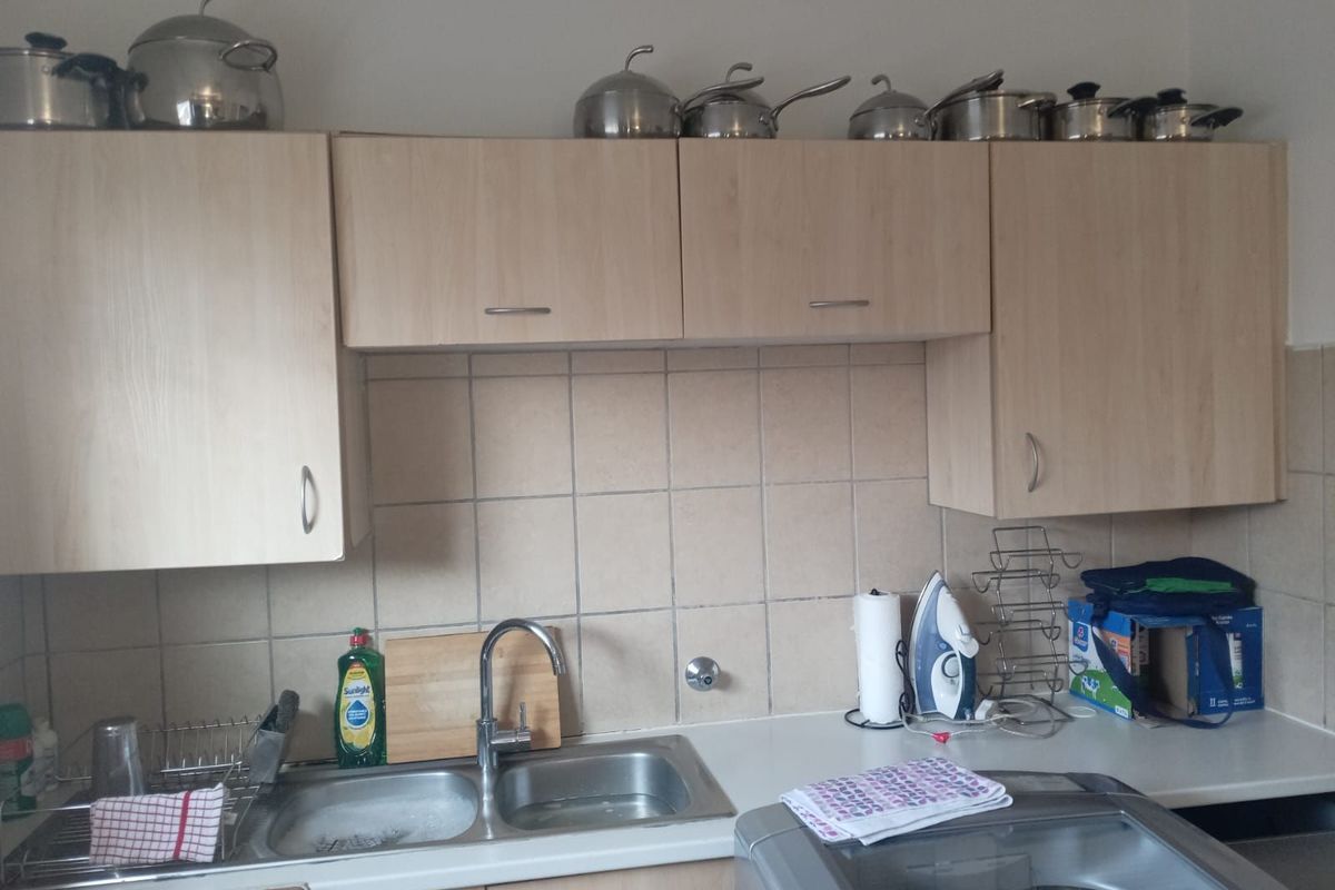 A functional kitchen area featuring light wood-finish cabinetry, a double-basin stainless steel sink, and tiled splashback.