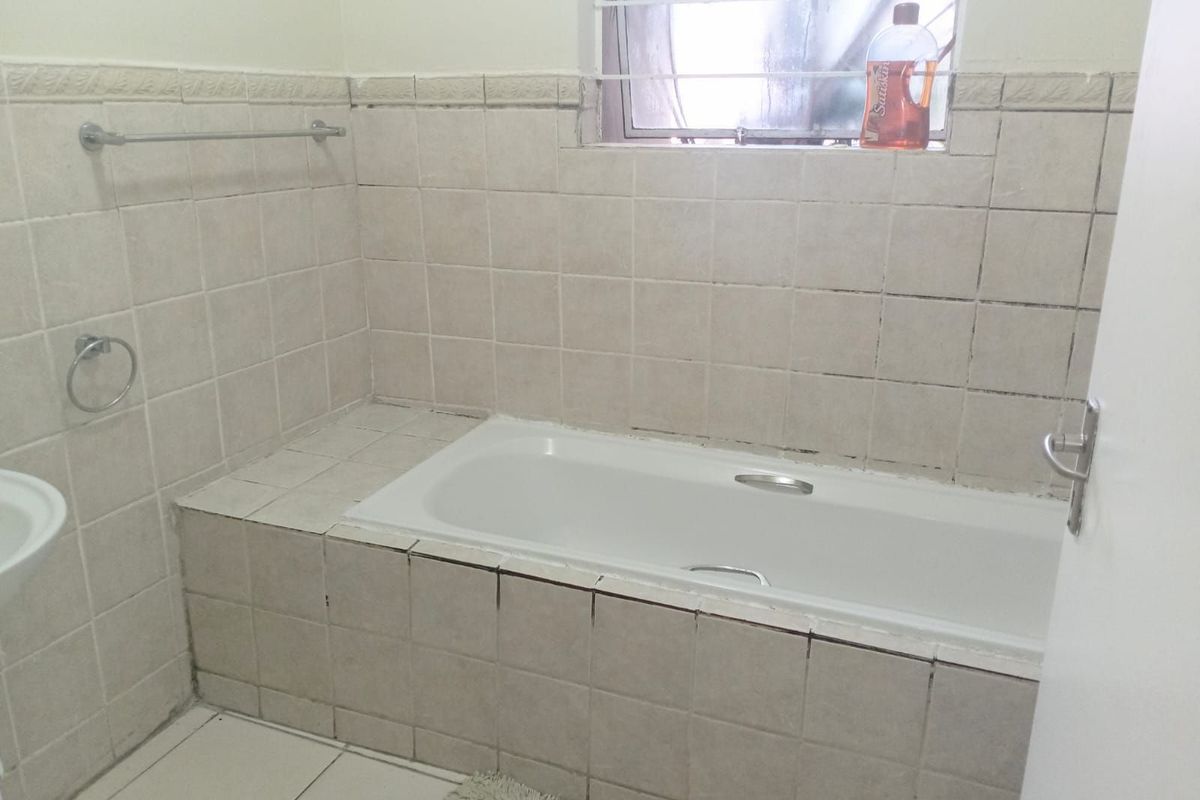 A functional bathroom featuring a built-in tiled bathtub, wall-mounted towel rail, and a window with security bars.