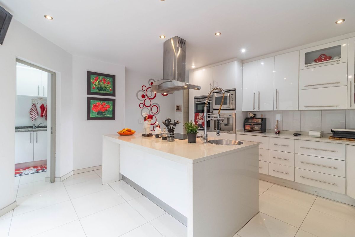 Modern kitchen featuring a central island, high-gloss cabinetry, integrated stainless steel appliances, and a separate scullery area.