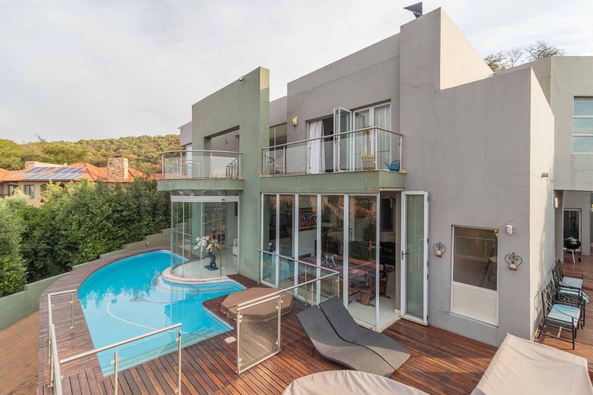 Rear view of a modern multi-level home featuring a swimming pool, wooden deck, glass-enclosed living areas, and upper-level balconies.