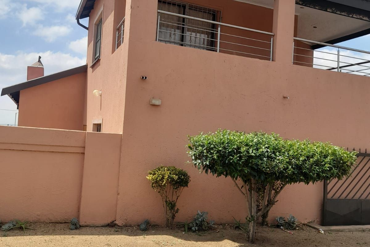 Exterior view of a two-story house featuring a balcony with metal railings and a perimeter boundary wall.