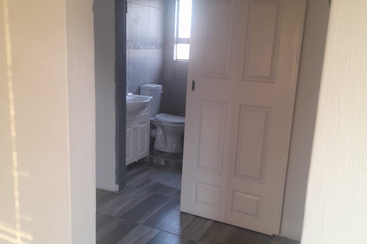 A view into a bathroom featuring tiled flooring, a vanity basin, and a toilet, accessed via a sliding door.