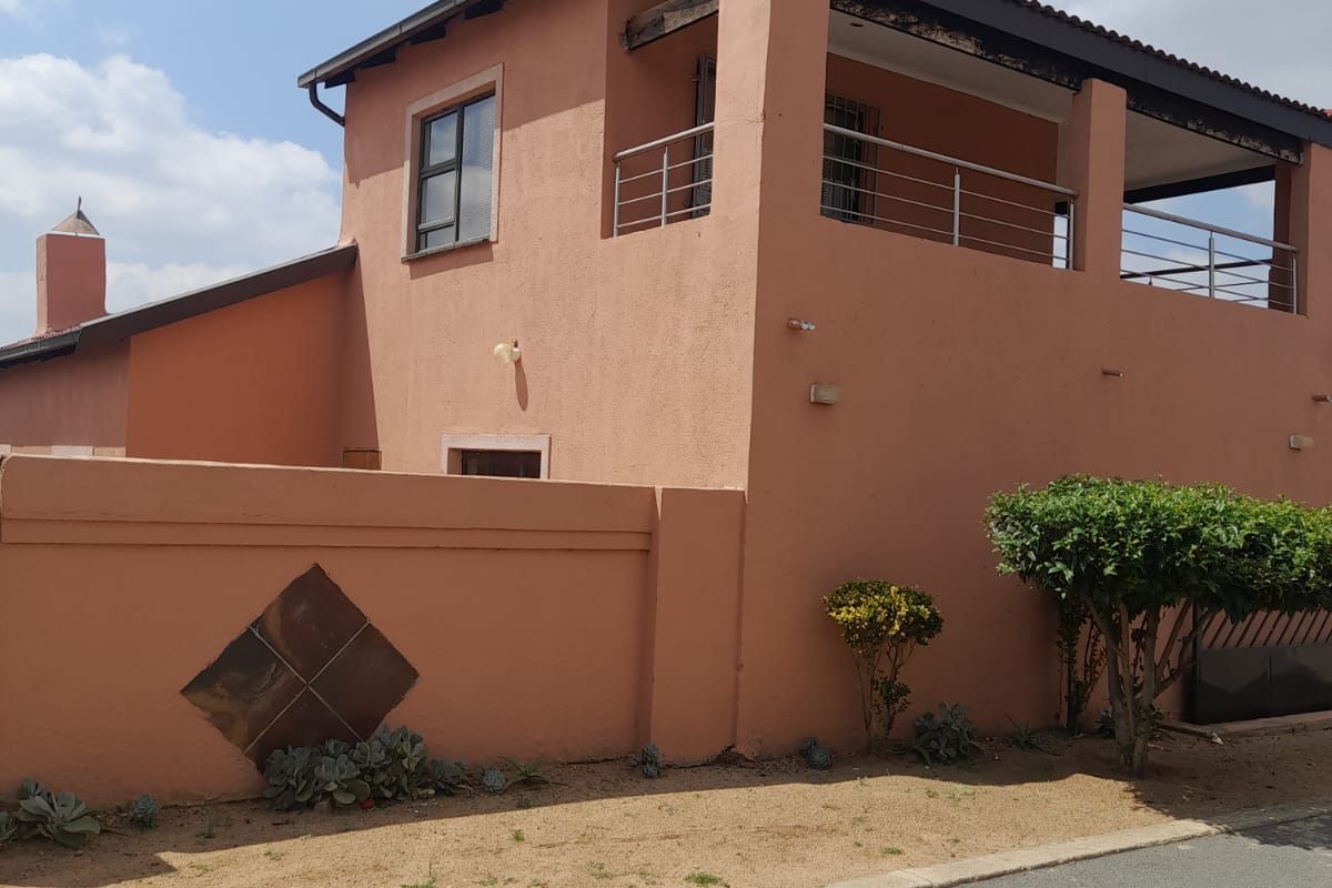 Exterior view of a two-story house featuring a balcony with metal railings, a perimeter boundary wall, and a tiled roof.