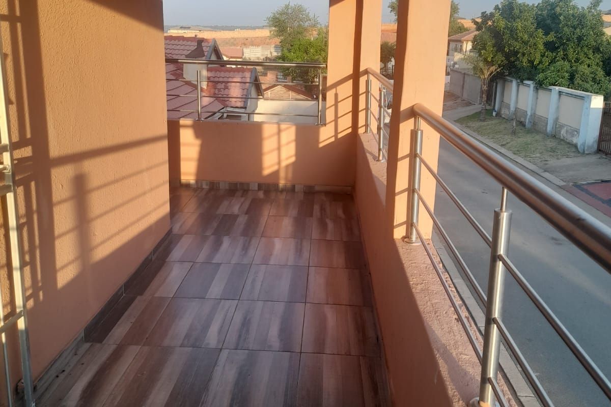 A covered balcony featuring wood-look tiled flooring and stainless steel railings, offering an elevated view of the surrounding neighborhood.
