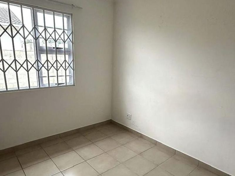 A vacant bedroom featuring neutral tiled flooring and a window fitted with a security gate.