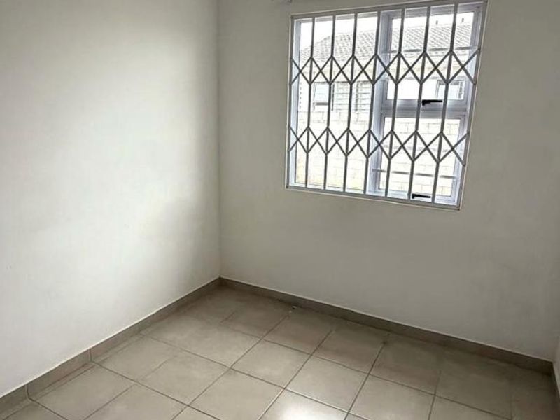 A clean, empty bedroom featuring neutral tiled flooring and a window fitted with security bars.