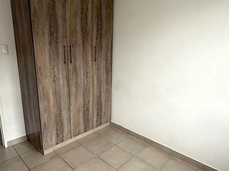 A simple bedroom featuring neutral tiled flooring and a functional built-in wooden wardrobe.