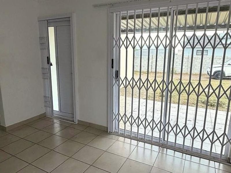 An empty living area featuring tiled flooring and a sliding glass door with security gates leading to the exterior.