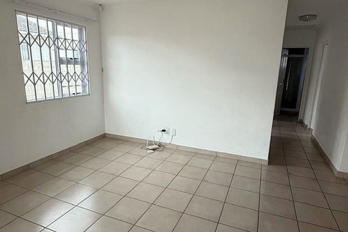 An empty living room featuring neutral tiled flooring and a window fitted with security bars, offering a clean, blank canvas for interior design.