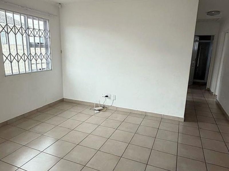 An empty living room featuring neutral tiled flooring and a window fitted with security bars, offering a clean, blank canvas for interior design.