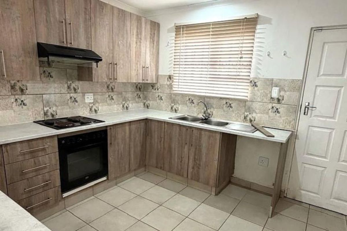 Functional kitchen featuring wood-look cabinetry, built-in oven, electric hob, extractor fan, and double bowl sink with tiled splashback and flooring.
