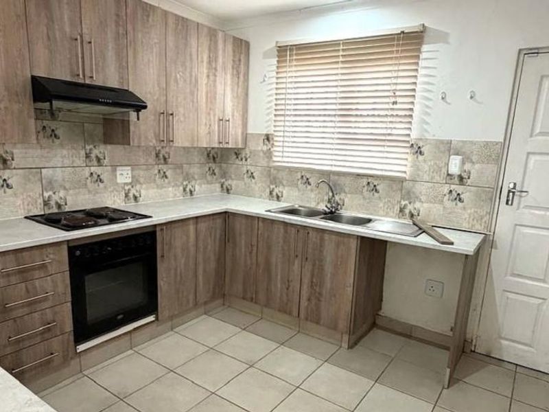 Functional kitchen featuring wood-look cabinetry, built-in oven, electric hob, extractor fan, and double bowl sink with tiled splashback and flooring.