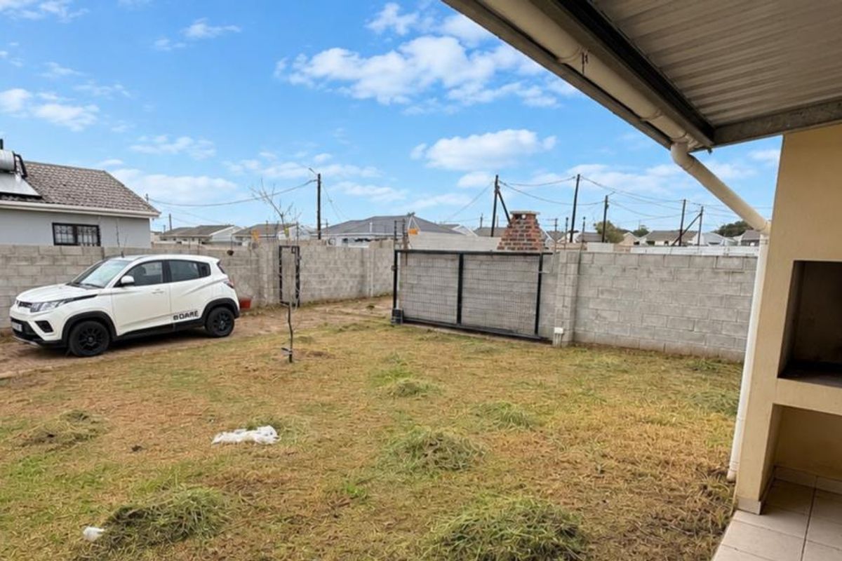 Rear garden area featuring a paved patio with a built-in braai, enclosed by concrete block boundary walls and a sliding gate.