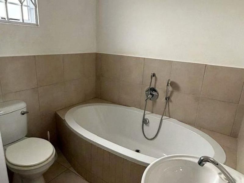 A functional bathroom featuring a built-in bathtub, pedestal basin, and toilet with neutral wall and floor tiling.