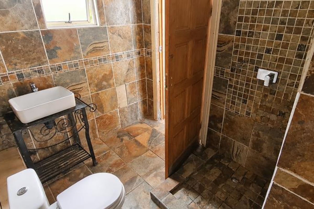 A compact bathroom featuring full-height stone-look wall tiling, a vessel sink on a metal stand, a toilet, and a walk-in shower area.