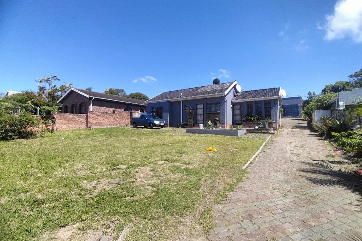 Rear view of the property featuring a large lawn, paved driveway, and brick boundary wall.