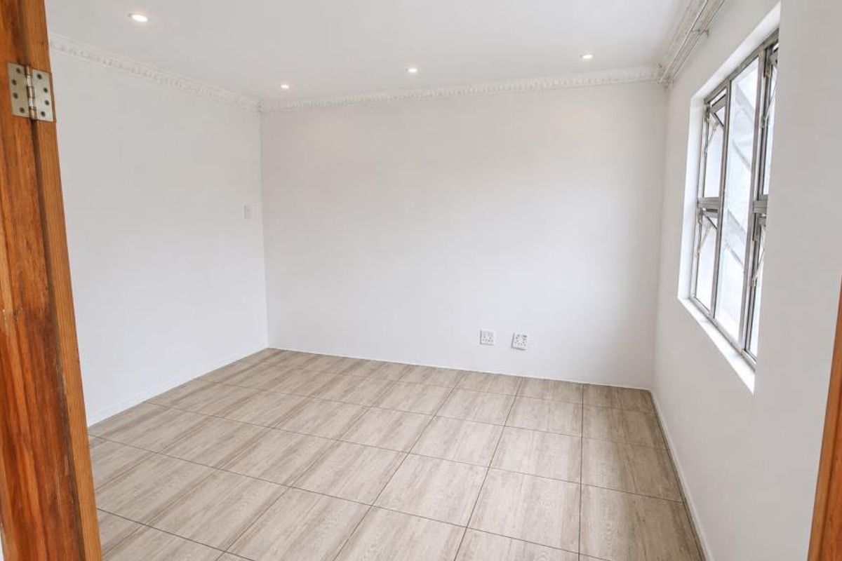 A bright, empty bedroom featuring neutral tiled flooring, recessed downlighting, and decorative ceiling cornicing, providing a clean and versatile living space.