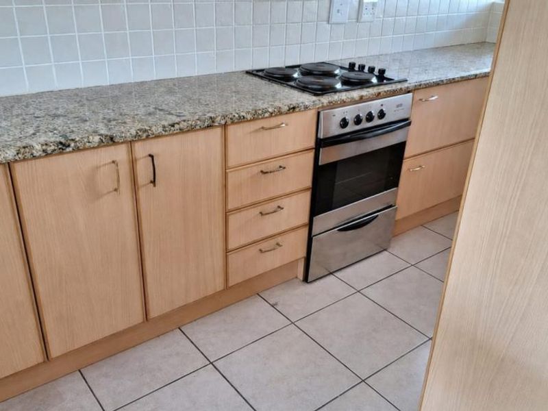 A functional kitchen featuring light wood laminate cabinetry, granite countertops, a built-in oven with an electric hob, and a tiled backsplash.