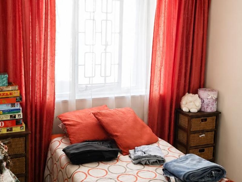 A compact bedroom featuring a window with integrated security bars, providing natural light and a functional layout for a small living space.