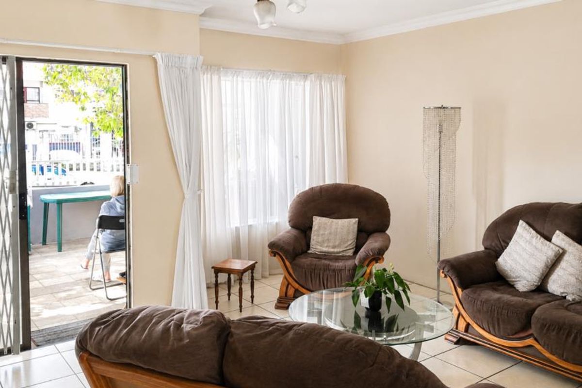 A bright living room featuring tiled flooring and a sliding door with a security gate, providing direct access to an outdoor patio area.