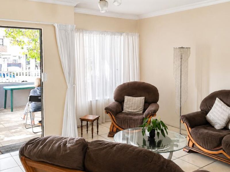 A bright living room featuring tiled flooring and a sliding door with a security gate, providing direct access to an outdoor patio area.