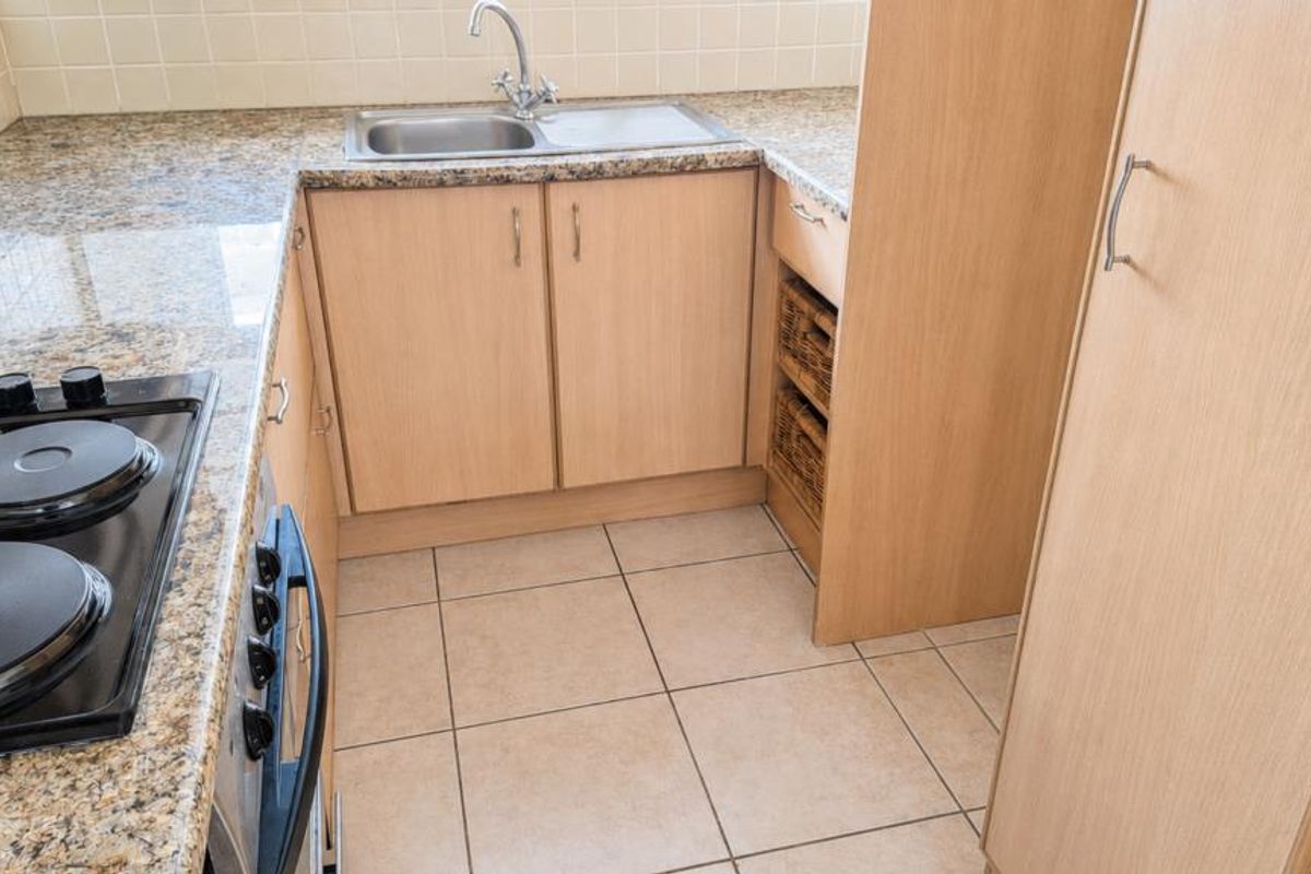 A compact kitchen featuring granite countertops, built-in cabinetry, an electric hob, and a stainless steel sink with tiled backsplash and flooring.