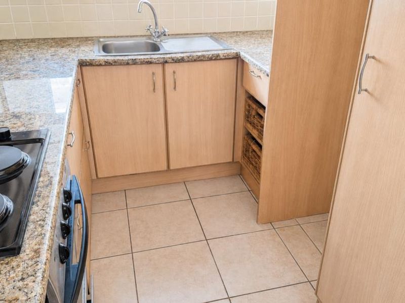 A compact kitchen featuring granite countertops, built-in cabinetry, an electric hob, and a stainless steel sink with tiled backsplash and flooring.