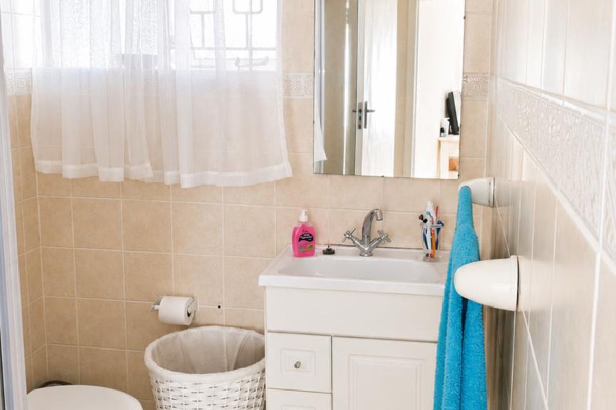 A functional bathroom featuring a vanity cabinet with a basin, wall-mounted mirror, toilet, and neutral ceramic wall tiling.