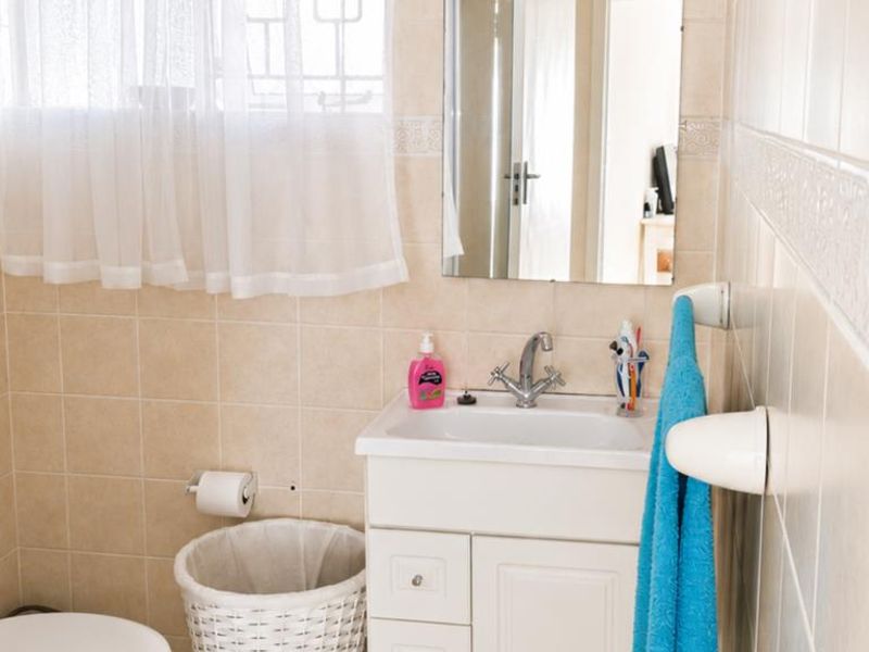 A functional bathroom featuring a vanity cabinet with a basin, wall-mounted mirror, toilet, and neutral ceramic wall tiling.