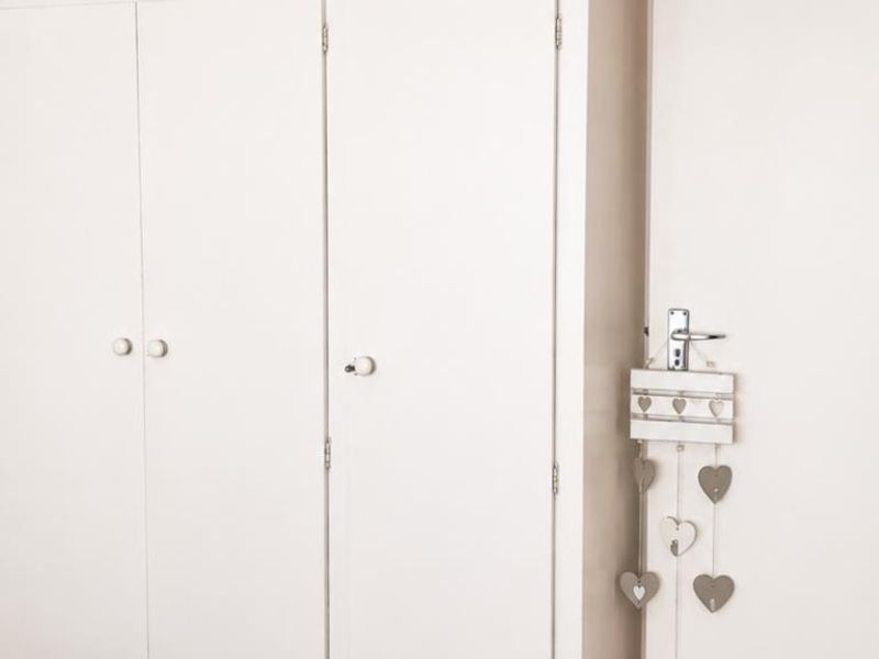 A bedroom interior featuring white built-in cupboards and a standard internal door.
