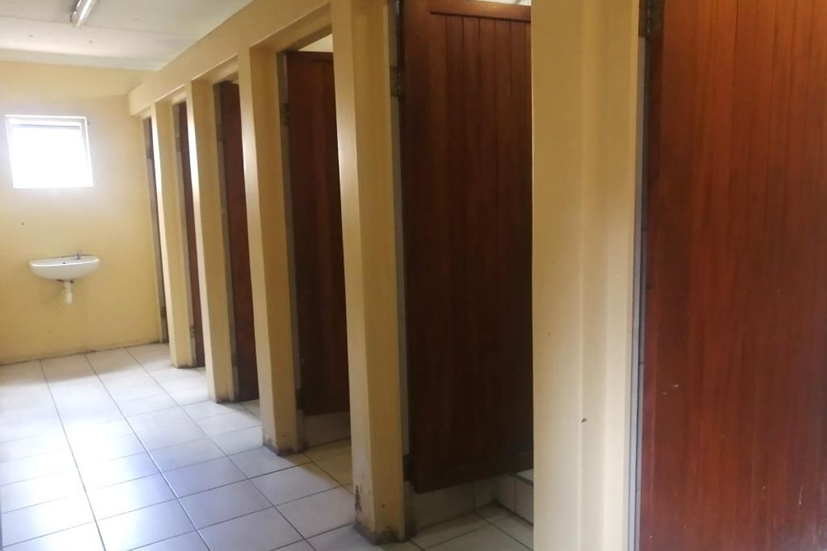 A communal bathroom facility featuring multiple individual stalls with wooden doors, tiled flooring, and a wall-mounted basin.
