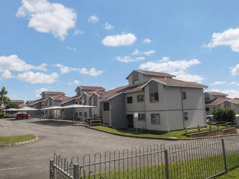 Exterior view of a multi-story apartment complex featuring paved parking areas, covered carports, and well-maintained building facades with tiled roofing.
