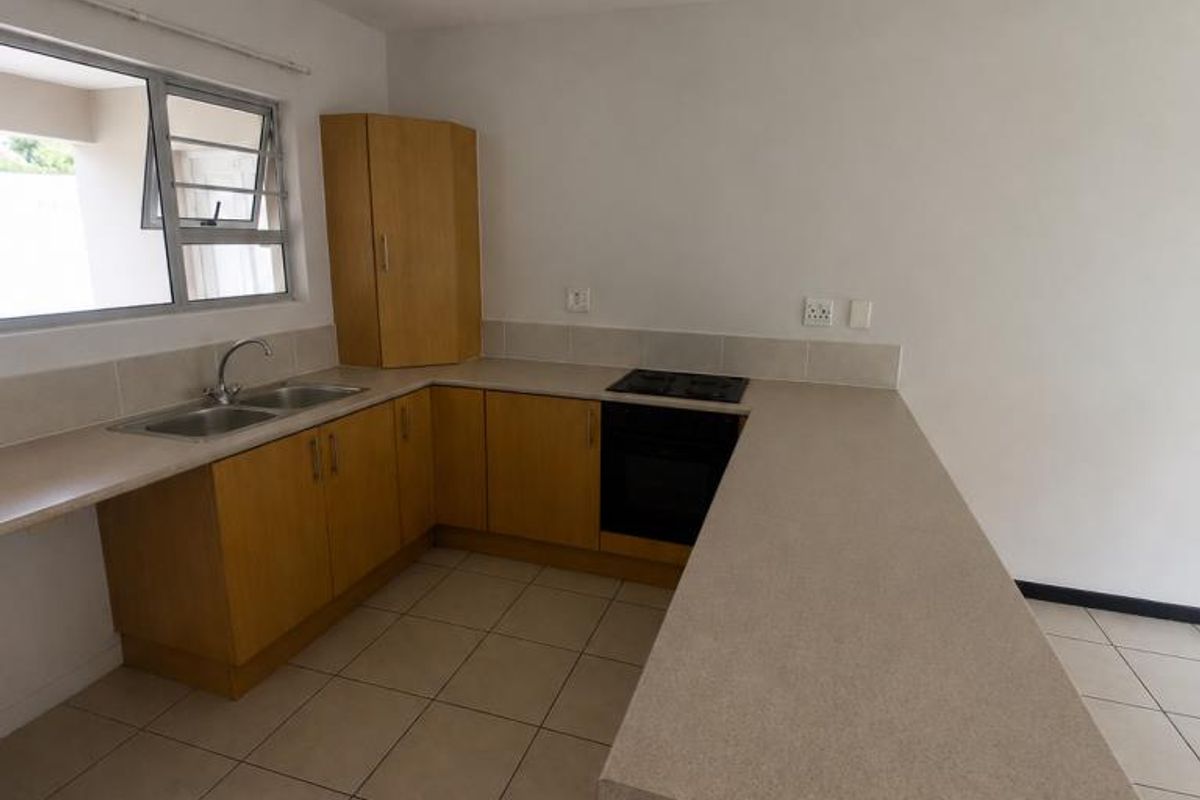 A functional kitchen featuring light wood cabinetry, stone-look laminate countertops, a built-in oven and hob, and neutral ceramic floor tiles.