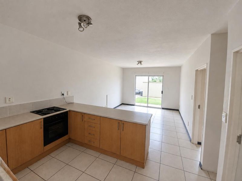 Open-plan kitchen and living area featuring tiled flooring, light wood cabinetry, built-in oven, and sliding door access to the rear exterior.