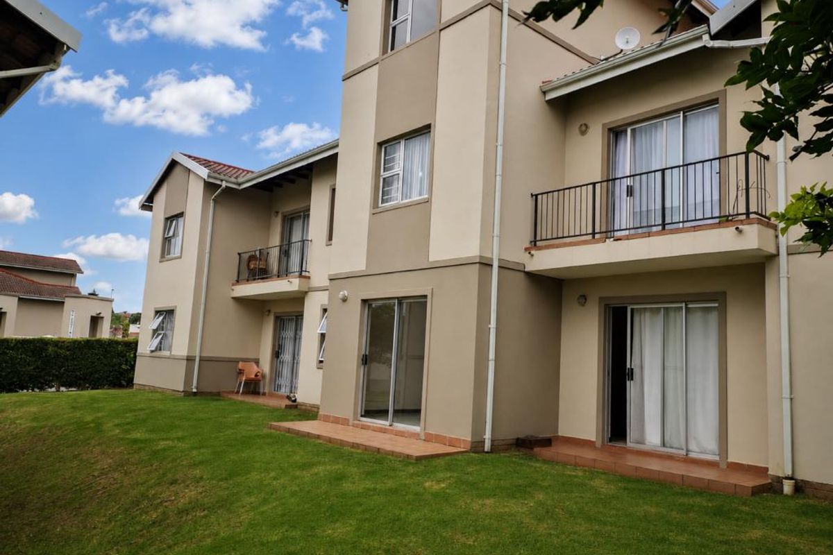 Rear view of a multi-story apartment building featuring ground floor tiled patios, upper-level balconies with metal railings, and sliding glass door access.