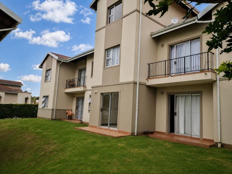 Rear view of a multi-story apartment building featuring ground floor tiled patios, upper-level balconies with metal railings, and sliding glass door access.